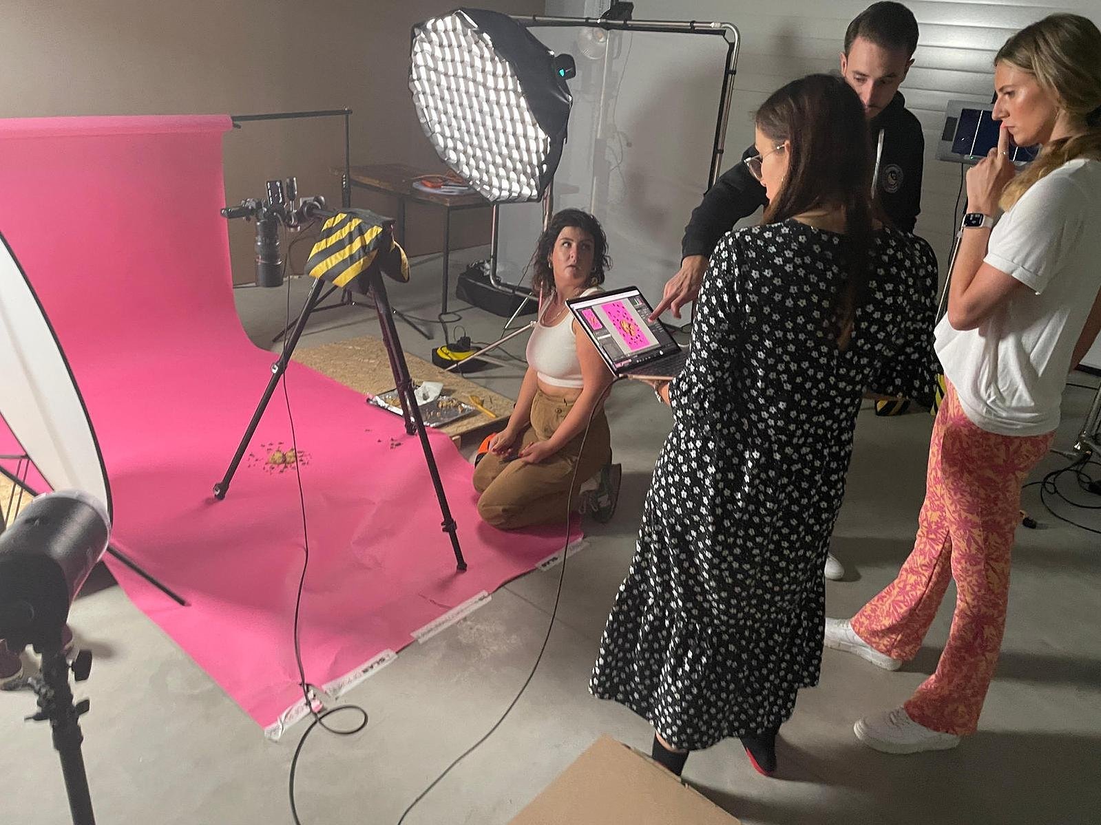 "Immerse yourself in the creative buzz of Georgie Glass Photography's studio with this candid shot of Georgie collaborating with her talented team. A vivid pink backdrop sets the stage for innovation and artistry, whilst on set in the studio.