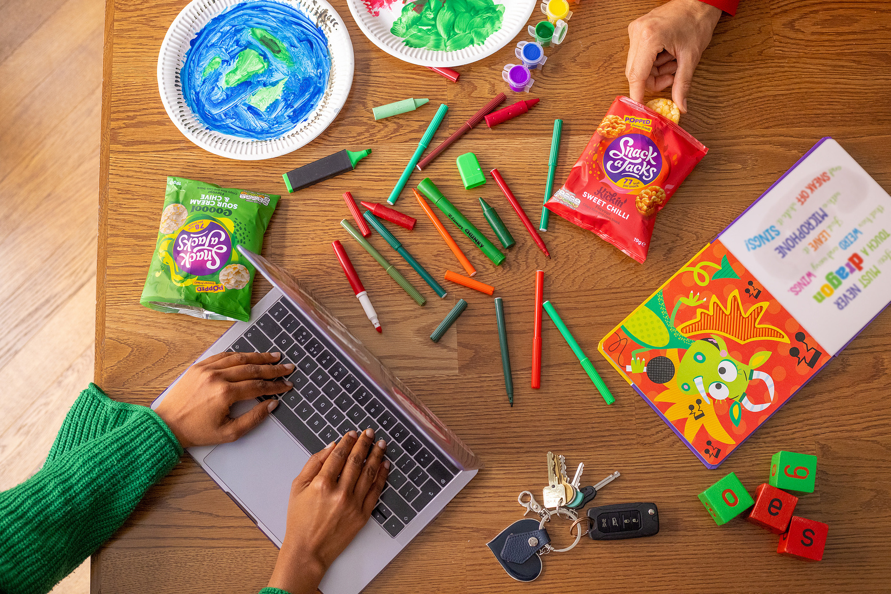 Manchester-based Georgie Glass Photography expertly blends food, product, and lifestyle photography in this vibrant image, showcasing crisp visual storytelling ideal for brands. Featuring an artful arrangement of snacks and creative tools beside a laptop.