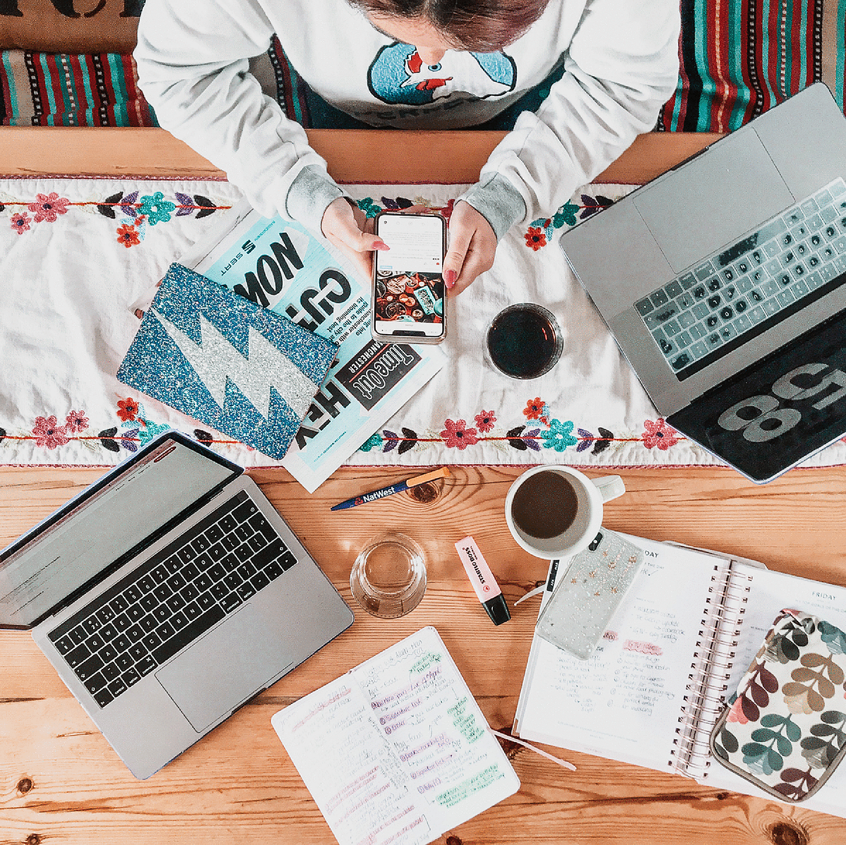 A girl works at her kitchen table, surrounded by her work items - coffee, laptop, notepads, pens, magazines - Georgie Glass Photography