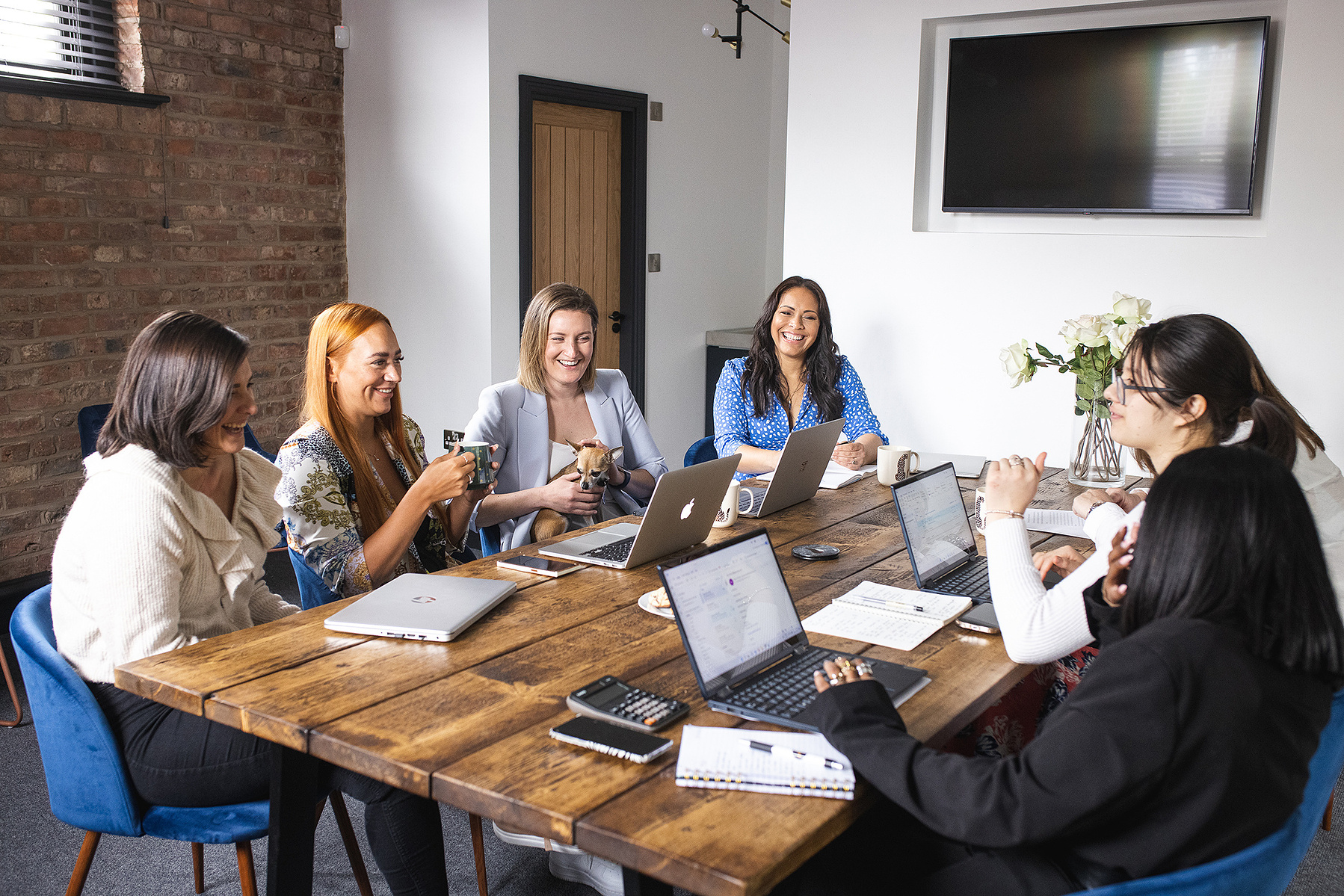 a team of women working and talking around a desk in an office