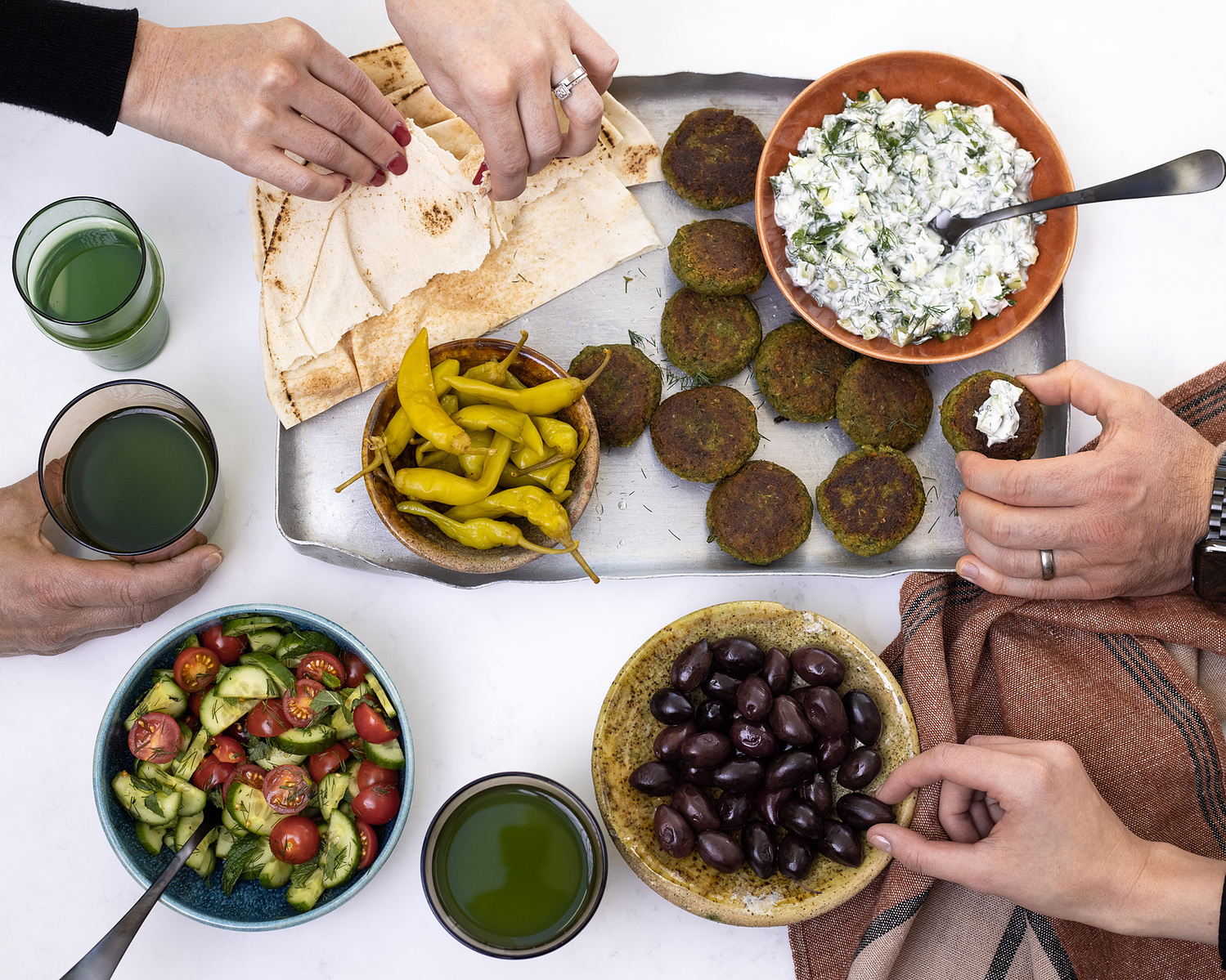 A colorful spread of Middle Eastern vegetarian dishes featuring falafel, tzatziki, pita bread, pickled peppers, cucumber-tomato salad, and olives, captured by Georgie Glass, food photographer in Manchester, UK.