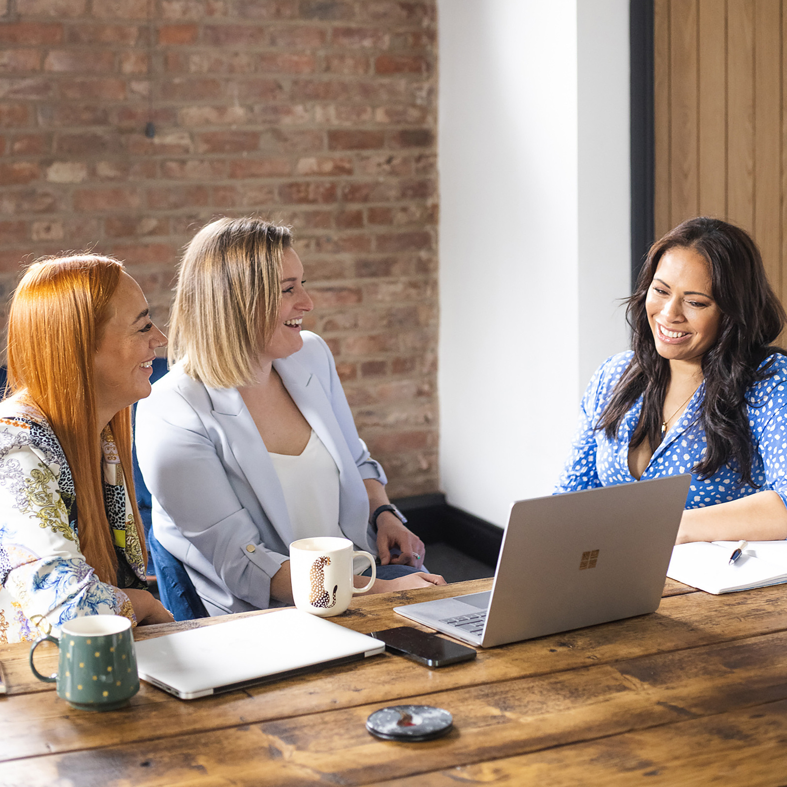 3 women at work sat around a desk talking with a laptop open. Portrait photography by Georgie Glass, Manchester photographer.