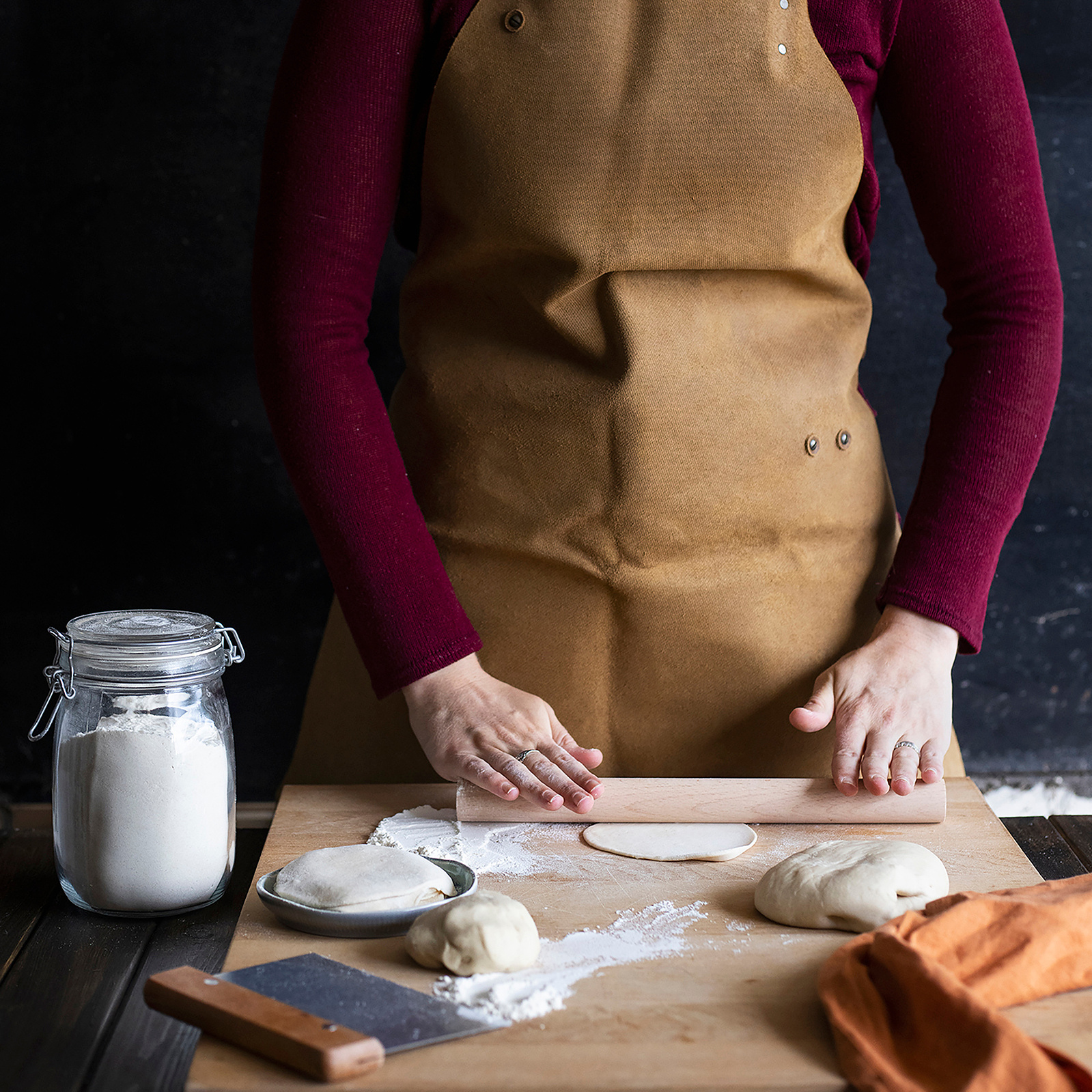 Georgie Glass Photography image of a baker wearing an apron rolling out dough on a table. Manchester photographer