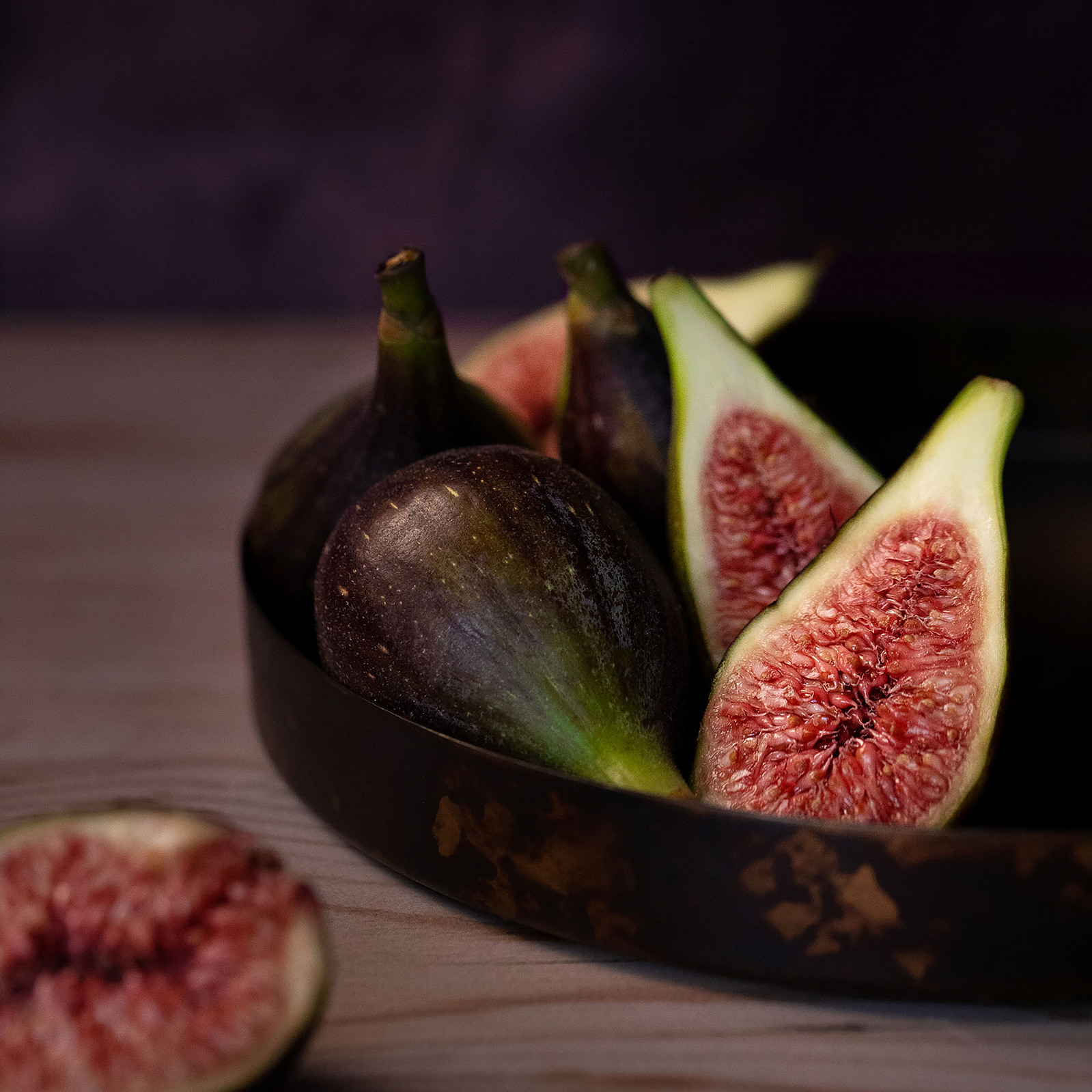 Close-up of ripe figs in a rustic bowl with one fig sliced open to reveal the juicy red interior, photographed by Georgie Glass, a Manchester, UK based food photographer, capturing the natural elegance of this humble ingredient.