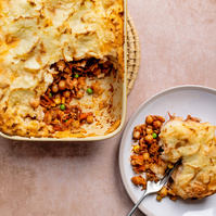 Freshly baked shepherd's pie in a white ceramic dish with a golden potato topping, portion scooped out onto a plate, showcasing the layers of seasoned meat, peas, and carrots, by Manchester food photographer Georgie Glass.