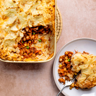Freshly baked shepherd's pie in a white ceramic dish with a golden potato topping, portion scooped out onto a plate, showcasing the layers of seasoned meat, peas, and carrots, by Manchester food photographer Georgie Glass.