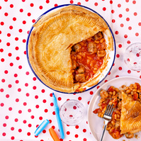 Overhead view of a homemade pie with a flaky crust, partially served, revealing a hearty bean and sausage filling, set against a playful red and white polka dot tablecloth, photographed by Georgie Glass in Manchester, UK.