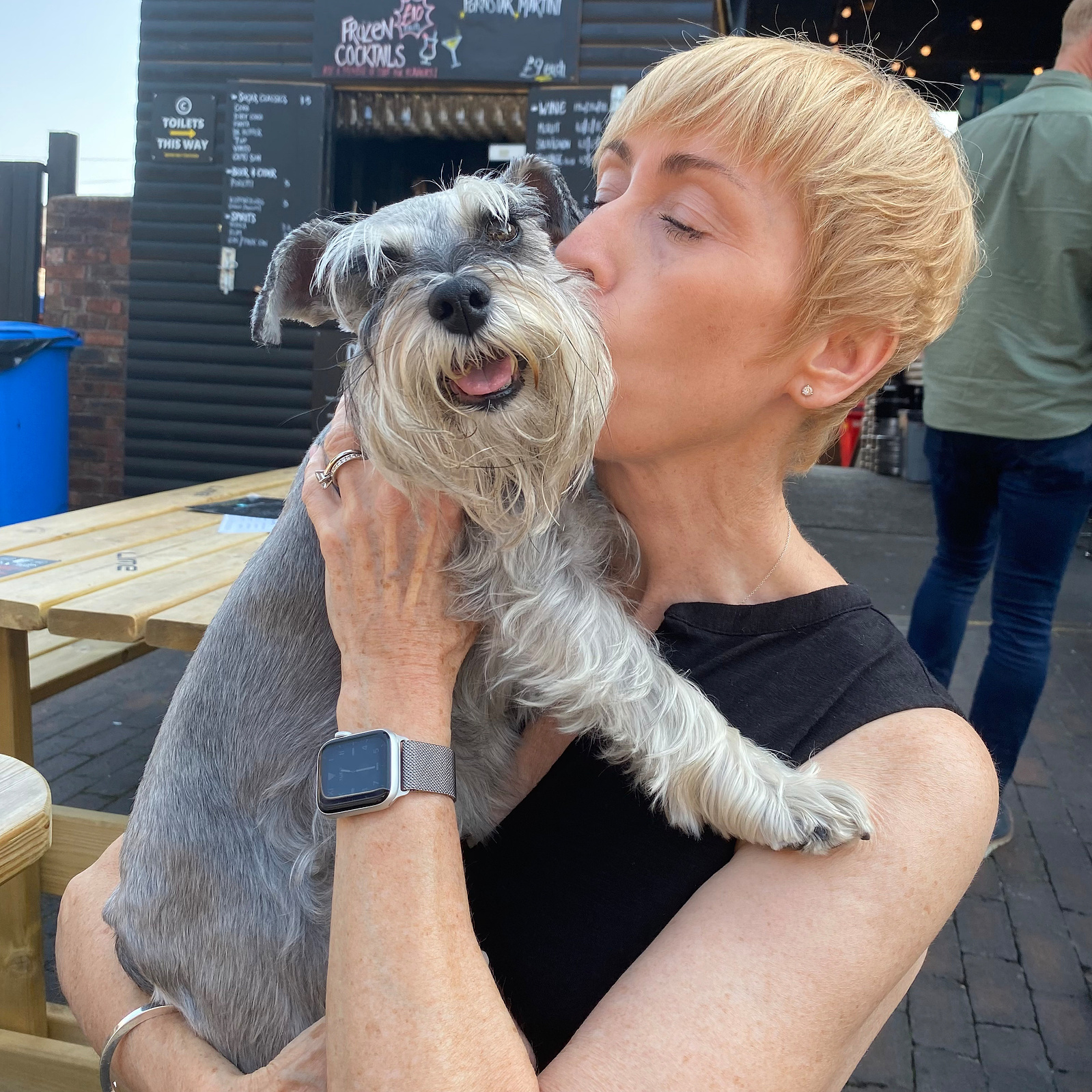 A woman with cropped blonde hair on a summers day kissing a very happy miniature schnauzer - Georgie Glass Photography