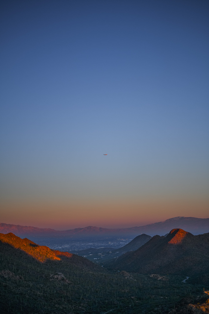 a passenger jet hangs suspended above the mountains in Arizona, illuminated by the dusk light