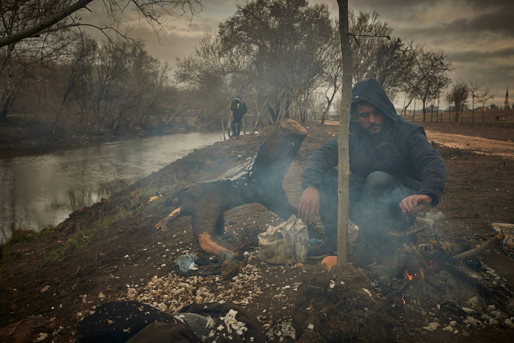 Saher, a Palestinian Refugee sits around a fire at dawn on the banks near the Edirne Old Bridge as they wait to cross into Greece and the European Union on March 05, 2020 in Edirne, Turkey.