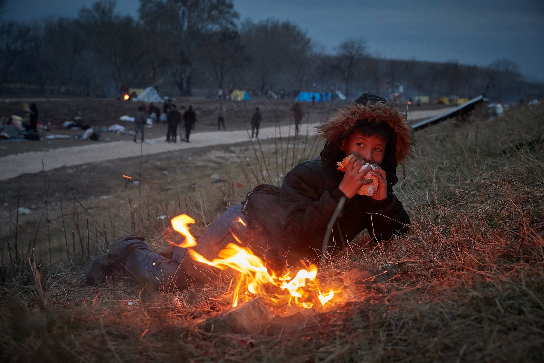 MARCH 5, 2020 - EDIRNE, TURKEY: A refugee from Afghanistan eats a sandwich whilst keeping warm by a fire in a makeshift camp on the banks of the river in Edirne as he and his family wait to cross into Greece and the European Union