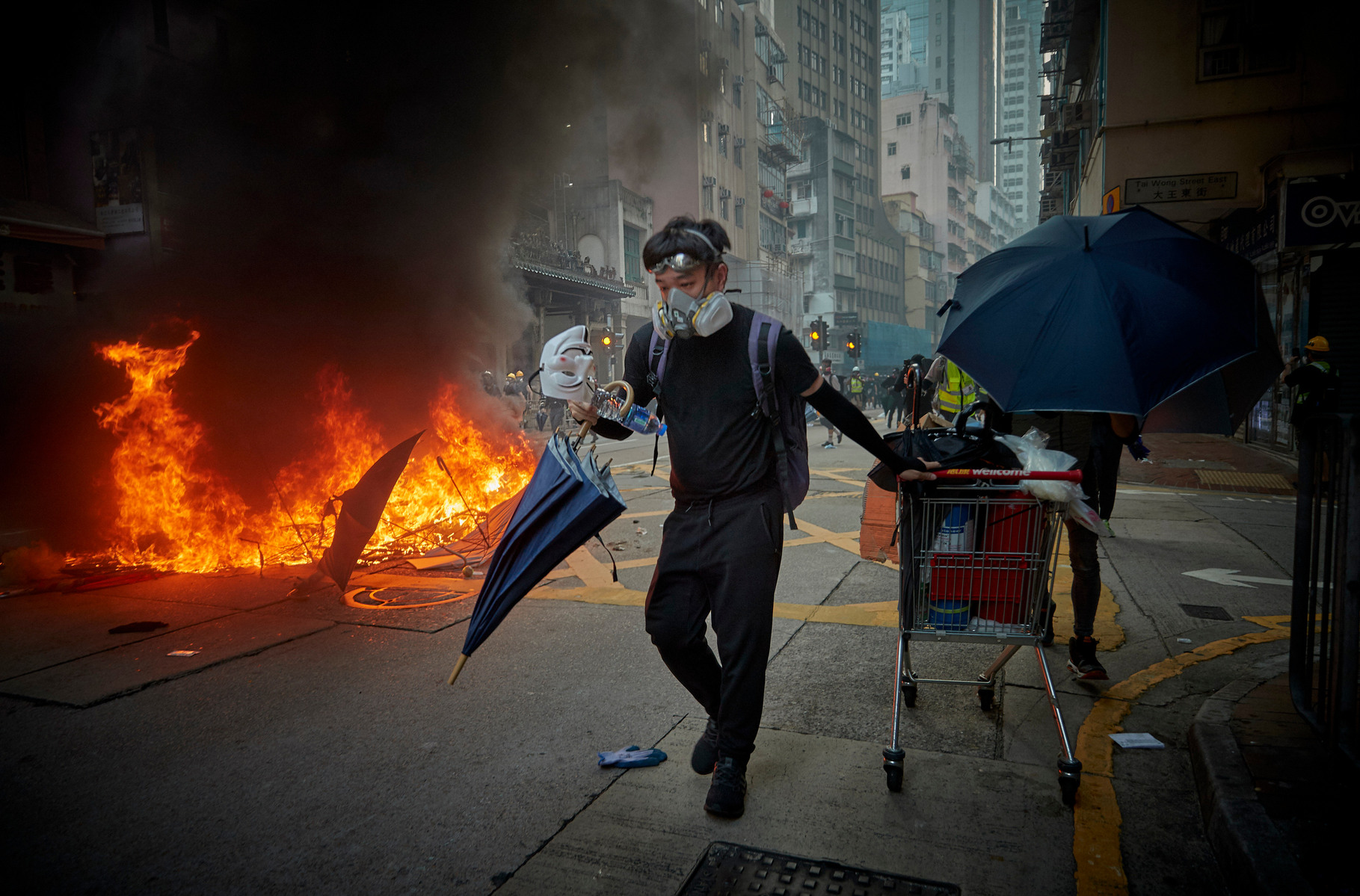OCTOBER 1, 2019: A Pro-democracy protestor pulls a shopping cart full of supplies past a burning barricade as protests to mark the 70th anniversary of the founding of the People's Republic of China turn violent.