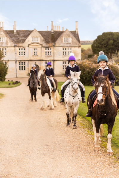 Four girls on ponies pose for a photograph in front of a grand school building that looks like a country house in England.
