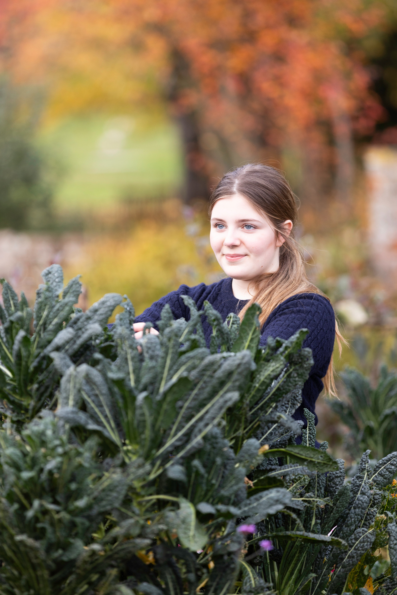 A girl stands in front of kale in a kitchen garden in England.