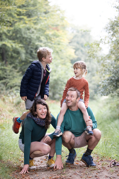 A family of four in Cranborne Chase Area of Natural Beauty. The mum crouches on the ground with her son on her shoulders. The father is crouching next to her with his daughter sitting on his shoulder. The boy is sticking his tongue out at his sister.