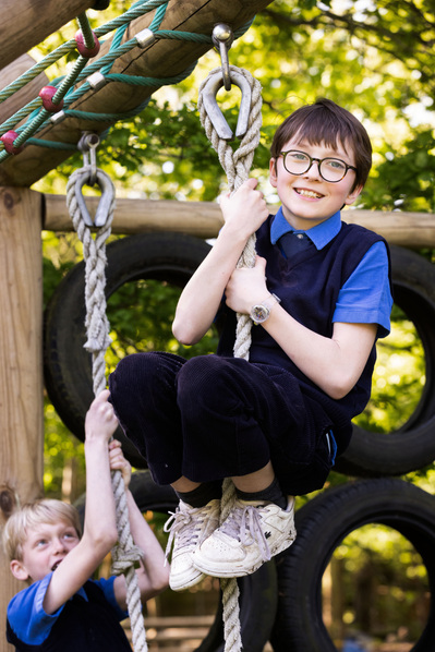 A boy at Sunningdale School, Ascot, Berkshire climbs a rope and smiles at the camera in School uniform and white trainers