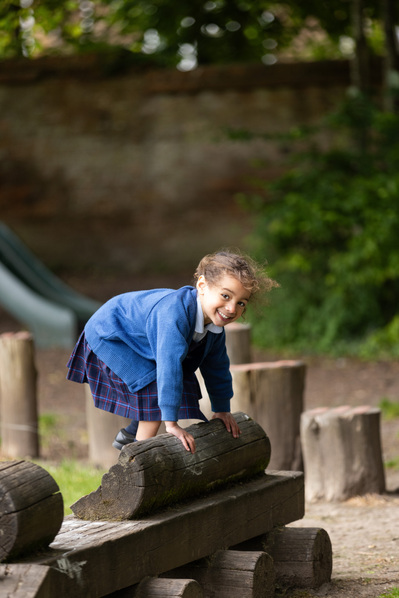 A nursery pupil at Chafyn Grove School, Salisbury tries to stand up on a log outside in the playground.
