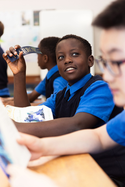 A young student holding a Harrow Bookmark looks at his friend. He's wearing school uniform at Sunningdale School, Ascot.