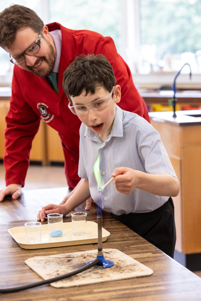 A pupil lights a bunsen burner with a green flame in a science lab at Chafyn Grove, Salisbury. His teacher is behind him.