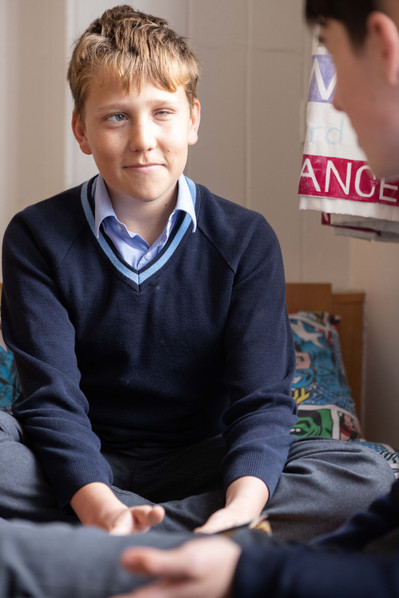 An 11 year old boarder at Clayesmore School, Dorset sits on his bed in his dormitory chatting to other students in his blue school uniform