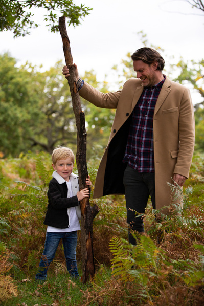 A Father and son stand holding a huge stick, taller than the Dad in the countryside. The son is looking at the camera and the Dad is looking proudly at the son.