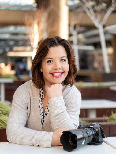 Amelia Johnson, a professional photographer poses for a portrait with a Canon mirrorless camera in front of her. 