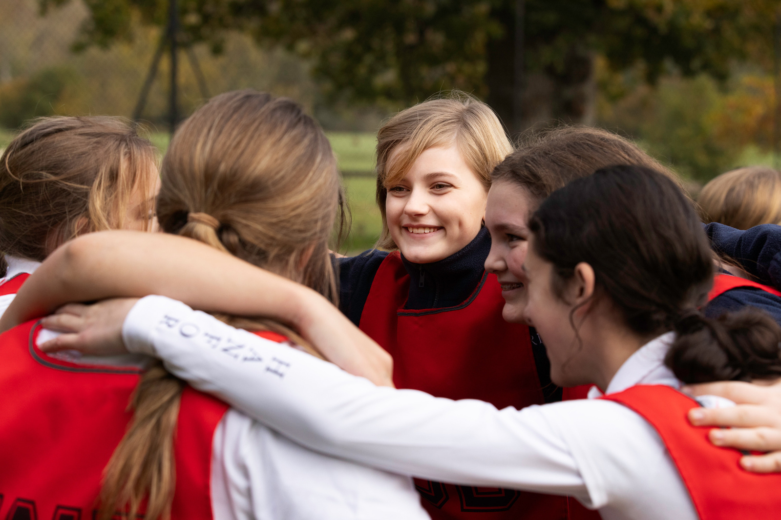 A group of pupils playing netball in a group huddle. Focus on one girl smiling excitedly before a match at an independent school in Somerset

