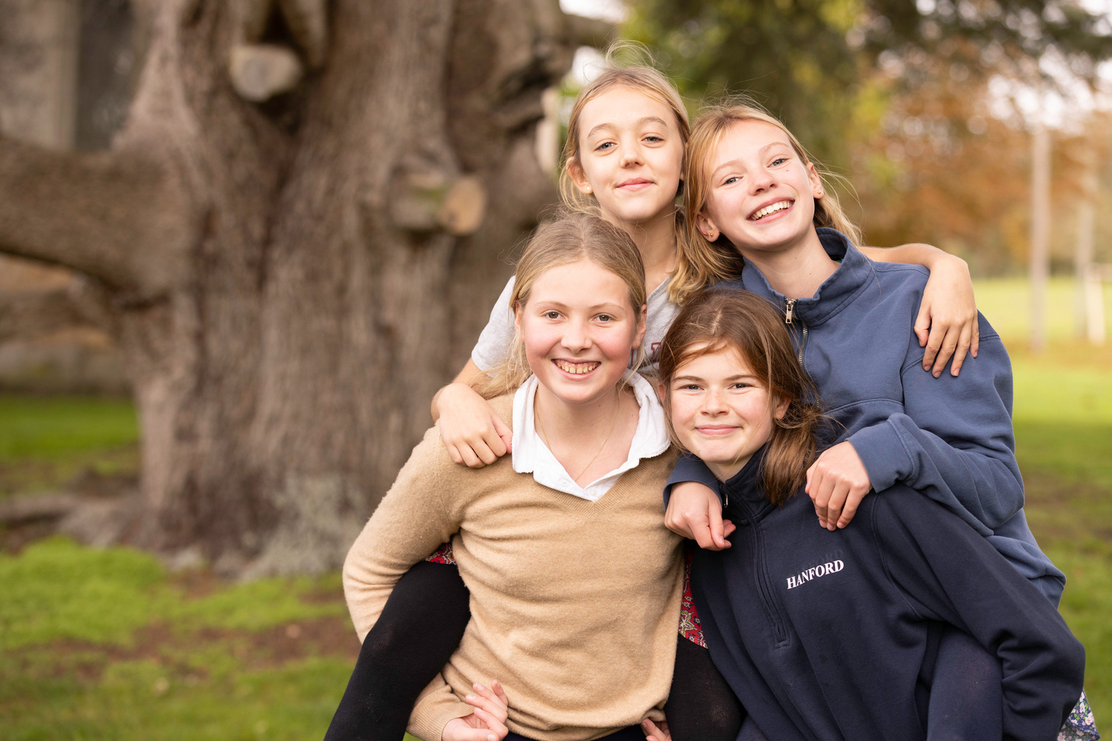 Four teenage girls in school uniform at a private school in Dorset stand in front of a tree.