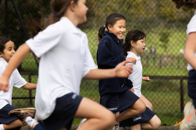 Girls laughing in sports kit as they run along a netball court skipping. Five students in the picture with the focus on the one in the middle.