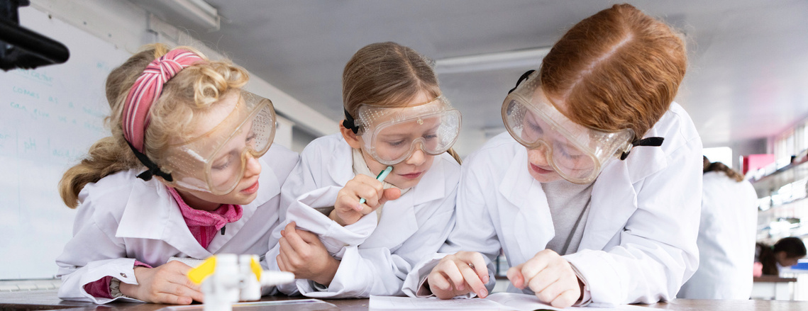 Three girls wearing lab goggles study their work in a science laboratory at an all girls independent school in Dorset.