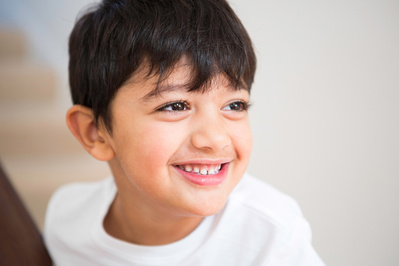 A boy sits on stairs at home in Bournemouth looking to his left. He's wearing a white tshirt.