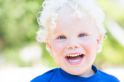 A three year old boy with white curly hair smiles at the camera at the beach in Bournemouth, Dorset