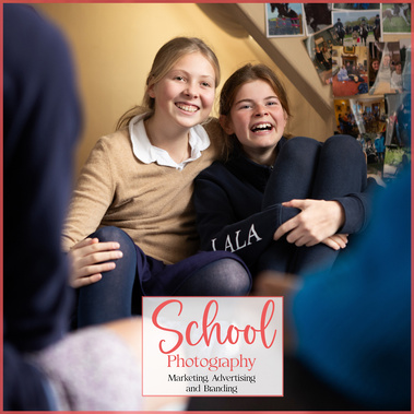 Two teenage school girls laughing in a dormitory at boarding school in Southern England. There are photos on the wall and they're wearing school uniform.