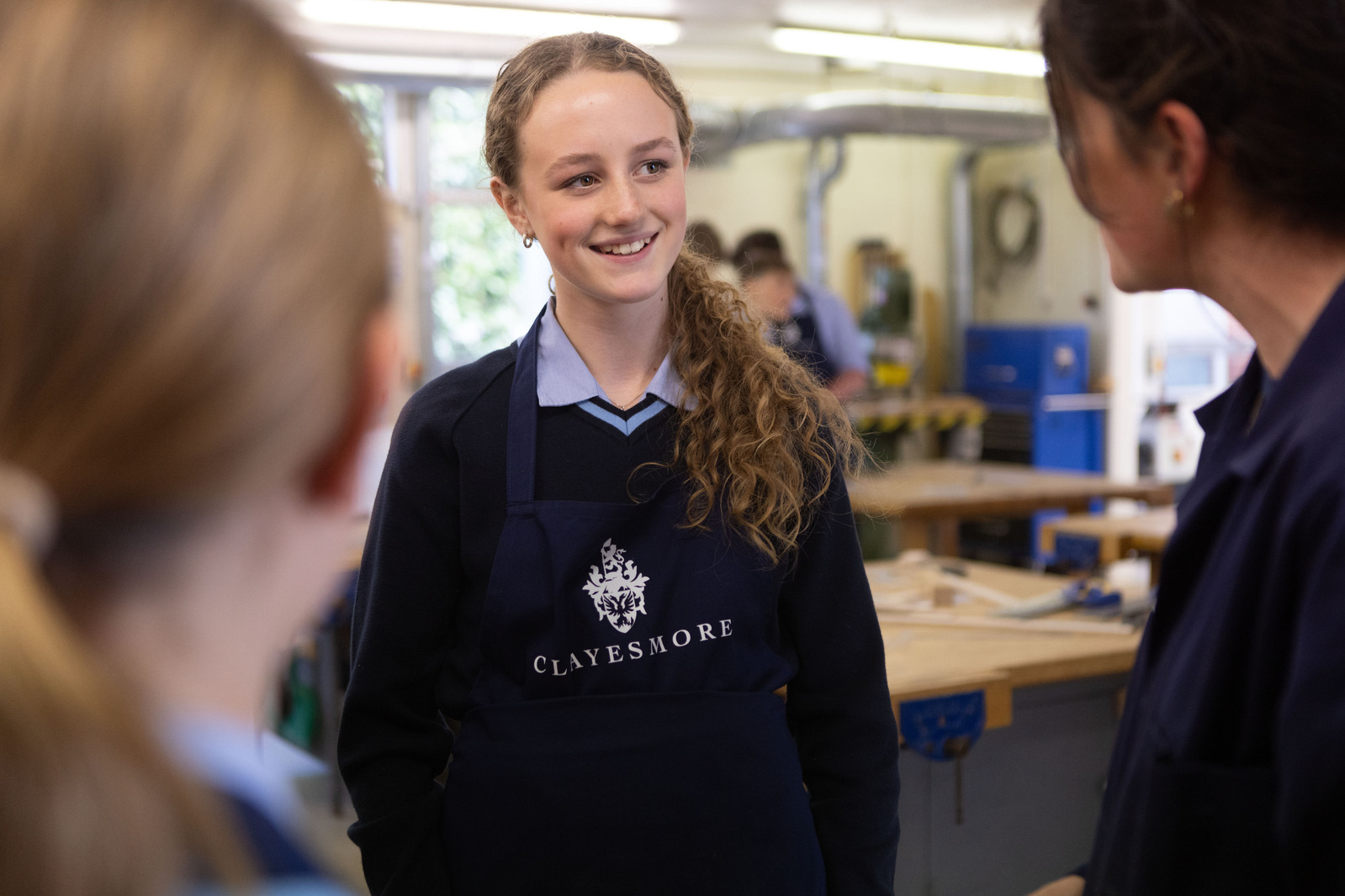 A girl in a Clayesmore School apron speaks to her teacher in the Design Technology Department.