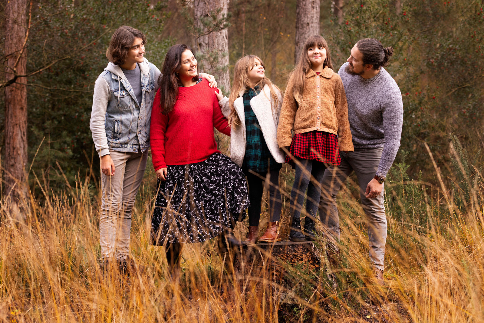 A family of five stand in a straight line behind some long grass at Moors Valley Country Park. They are all looking at the 10 year old daughter who is grinning at the camera. 