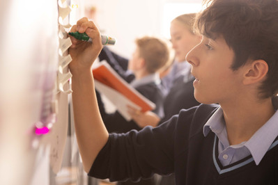 A boy at Clayesmore School, Dorset writes on the white board in his classroom. He's wearing school uniform