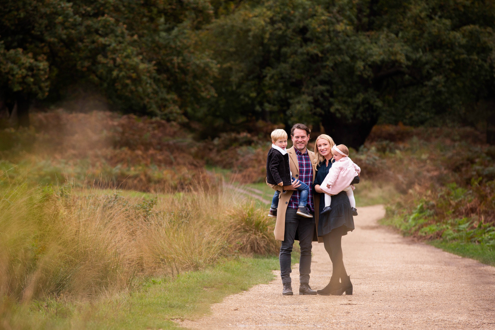 A beautiful young family stand on a pathway in Avon Heath posing for a photo. The parents are holding their 5 year old son and 2 year old daughter.