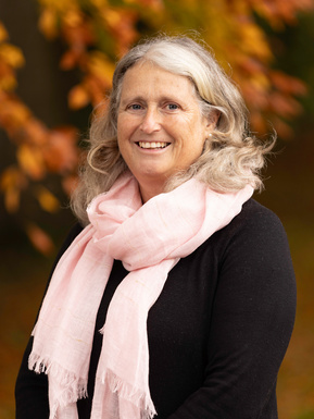 A teacher poses for a corporate portrait in front of an autumnal tree. She is smiling and wearing a pink scarf. She is the deputy head teacher at Hanford School, Child Okeford, Dorset