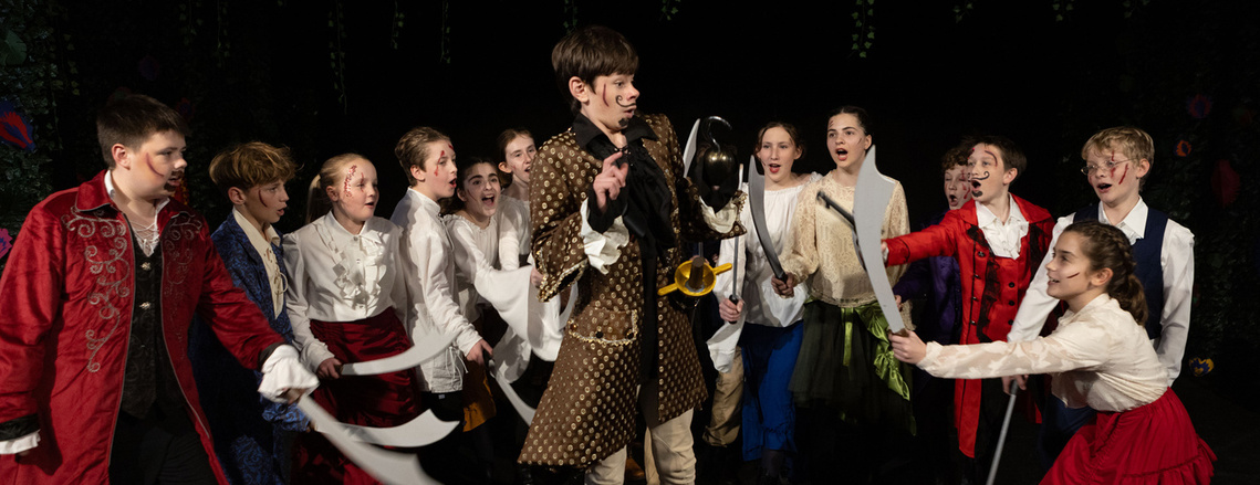 A group of students at Clayesmore, Dorset, act out the play Peter Pan. Hook is standing in the middle being threatened by a sword.