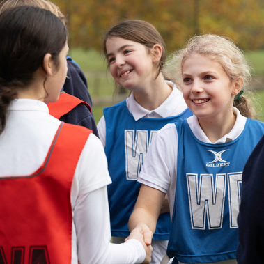 A young netball player wearing a wing attack bib shakes hands with her opponent. She is on a netball court in Southampton, Hampshire and she's smiling. 