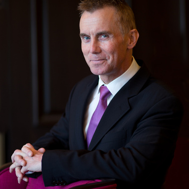 Gary Rhodes poses for a photograph in a smart black suit and a purple tie.