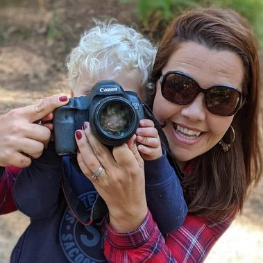 Amelia Johnson Photographer holds a professional camera up to her son's eye in a park in Sherborne, Dorset