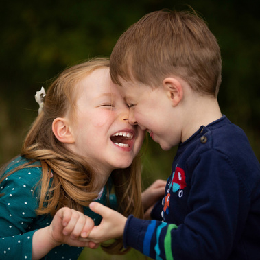 Two five year old twins laughing in a park in Sherborne, England. Their foreheads are touching.