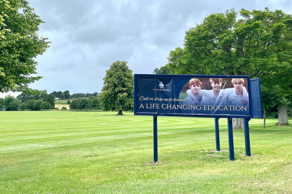 A photograph of a billboard advertising Clayesmore School, North Dorset, with three boys in cricket whites.