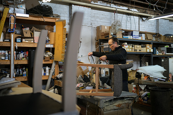 upholsterer Jason Shen working in upholstery workshop surrounded by chairs and tools