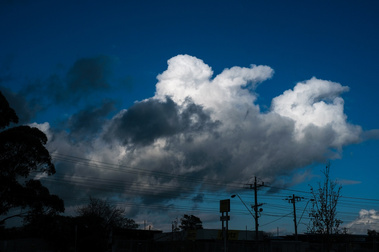 dramatic clouds and blue sky with power poles and lines and buildings silhouetted