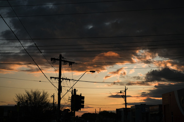 a suburban street scene with big sunset sky,  with power lines and poles and a traffic light 