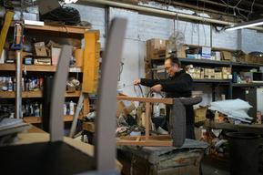 upholsterer Jason Shen working in upholstery workshop surrounded by chairs and tools
