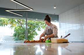 pastry chef Matilda Smith in apron making almond croissants at Penny for Pound workroom with white tiles and a big marble bench and a big window looking through to green tree