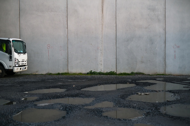 a close up  concrete slab wall  with gravel and puddles on the ground and a white truck in the left of the frame